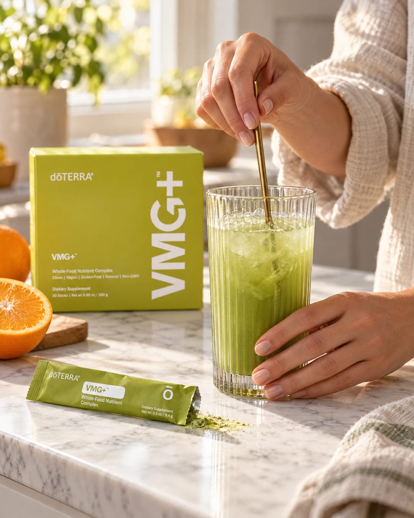 Hands stirring a tall ribbed glass of the green VMG+ drink on a sunlit marble counter, the box and an open stick packet beside it