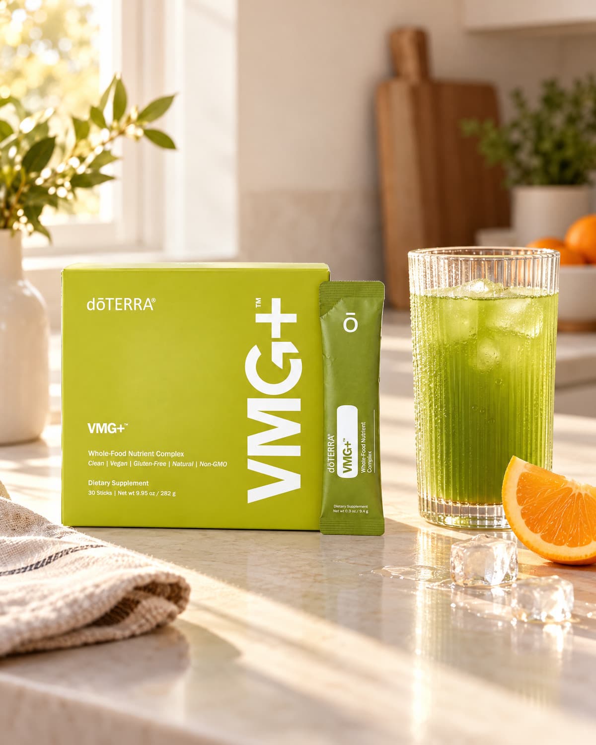 VMG+ box and stick next to a tall glass of the green drink on ice, with an orange slice